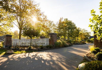 Entrada a Wellness Lodge en Hof van Salland, Países Bajos, con árboles verdes y luz solar al atardecer.