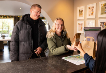 Un couple s'enregistre à la Wellness Lodge de Hof van Salland aux Pays-Bas et reçoit un sac de bienvenue.