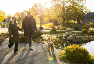 Coppia che passeggia col cane vicino allo stagno alla Wellness Lodge, Hof van Salland, Paesi Bassi, sole.