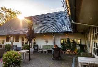 Patio exterior de Wellness Lodge en Hof van Salland, Países Bajos, con mesas, brasero y luz del atardecer.