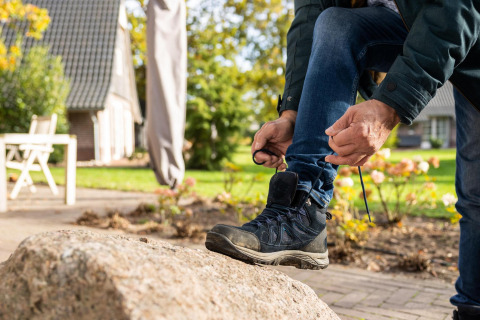 Persona atando sus botas de senderismo sobre una roca frente a Wellness Lodge en Hof van Salland, Países Bajos.