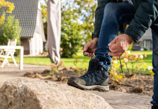 Une personne lace ses bottes de randonnée sur une pierre devant le Wellness Lodge à Hof van Salland, Pays-Bas.