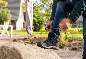 Persona atando sus botas de senderismo sobre una roca frente a Wellness Lodge en Hof van Salland, Países Bajos.