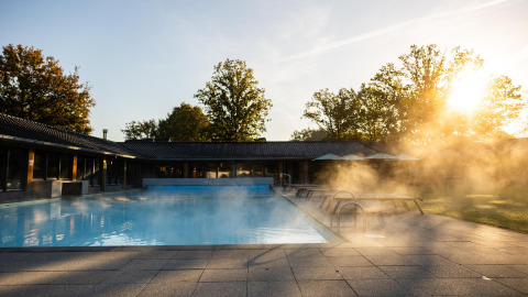 Udendørs opvarmet pool med damp ved solopgang ved Wellness Lodge, Hof van Salland, Nederlandene.