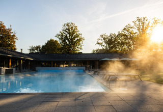 Piscina exterior climatizada con vapor al amanecer en Wellness Lodge, Hof van Salland, Países Bajos.