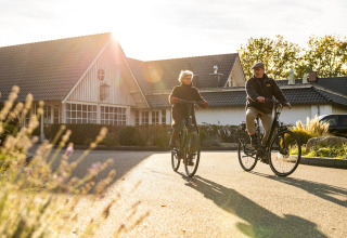 Dos adultos mayores en bicicleta frente a la Wellness Lodge en Hof van Salland, Países Bajos, al sol.