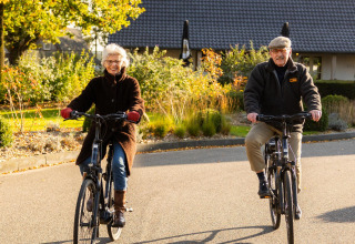 Pareja mayor en bicicleta frente a la tiny house Wellness Lodge en Hof van Salland, Países Bajos.
