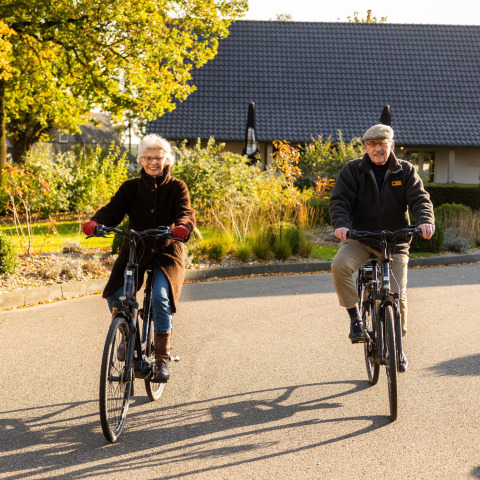 Coppia anziana in bicicletta davanti alla tiny house Wellness Lodge a Hof van Salland, Paesi Bassi.