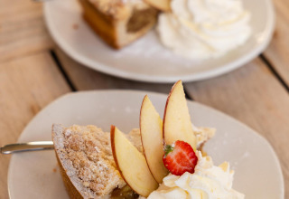 Dos platos con tarta de manzana, nata montada, rodajas de manzana y fresa en Wellness Lodge, Hof van Salland.
