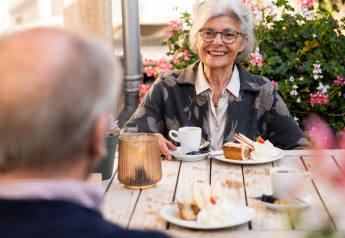 Pareja mayor disfruta café y pastel al aire libre en Wellness Lodge, Hof van Salland, rodeados de flores.