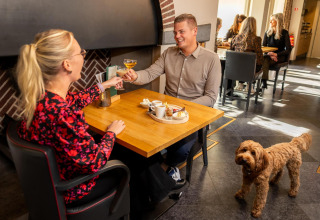 Pareja disfruta de bebidas y postre en una mesa, con un perro marrón cerca en Wellness Lodge, Hof van Salland.