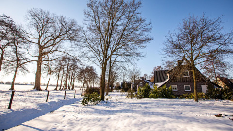 Vinterbillede af Wellness Lodge ved Hof van Salland i Holland, omgivet af sne, træer og blå himmel.