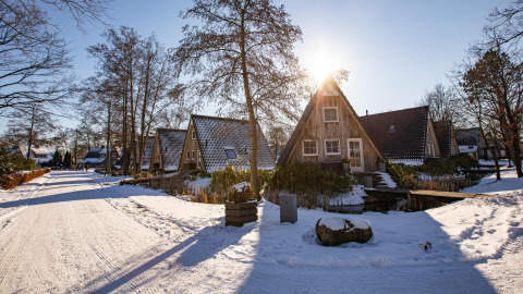 Solrig vinterdag ved Wellness Lodge, Hof van Salland, med små hytter og sneklædte omgivelser i Holland.