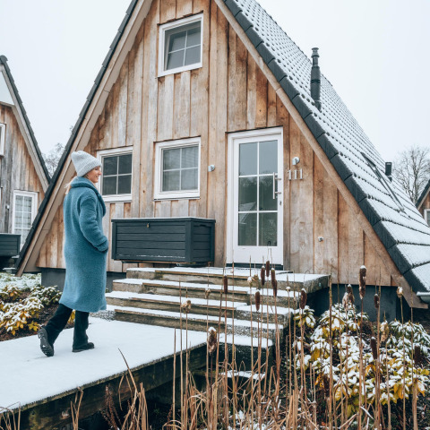 Kvinde med blå frakke går foran Wellness Lodge tiny house i Hof van Salland, Holland, om vinteren.