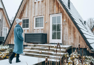 Donna con cappotto blu cammina davanti alla tiny house Wellness Lodge a Hof van Salland, Paesi Bassi, in inverno.