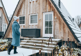 Donna con cappotto blu cammina davanti alla tiny house Wellness Lodge a Hof van Salland, Paesi Bassi, in inverno.