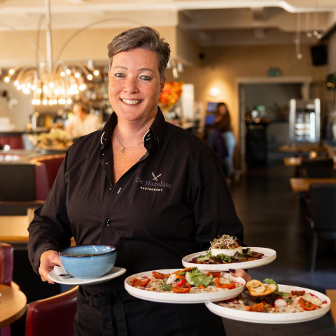 Cameriera sorridente serve piatti colorati al ristorante De Hazelaer, Wellness Lodge, Hof van Salland, Paesi Bassi.