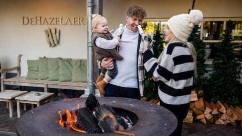 Familie hygger sig ved bålplads foran Wellness Lodge ved Hof van Salland, DeHazelaer, i Holland.