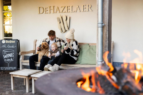 Familie med hund nyder hygge udenfor Wellness Lodge ved Hof van Salland, Holland, foran bål.
