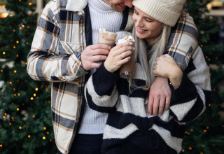 Pareja disfrutando chocolate caliente junto a árboles de Navidad en Wellness Lodge, Hof van Salland, Países Bajos.