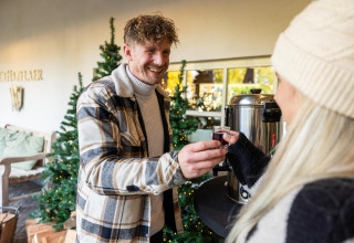 Dos personas comparten una bebida caliente junto a árboles de Navidad en Wellness Lodge, Hof van Salland, Países Bajos.