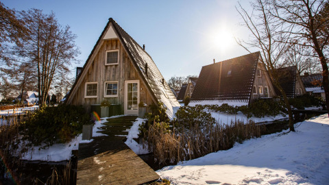 Et lille A-formet træhus med sne omkring ved Wellness Lodge i Hof van Salland, Holland, på en solrig dag.