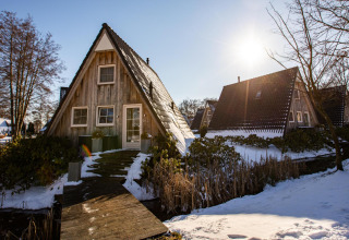 Piccola casa in legno a forma di A sulla neve al Wellness Lodge, Hof van Salland, Paesi Bassi, giornata di sole.