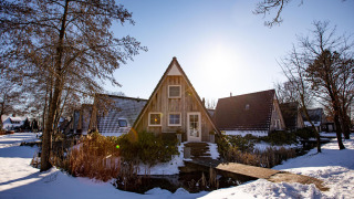 Casa pequeña Wellness Lodge cubierta de nieve en Hof van Salland, Países Bajos, con árboles al sol invernal.