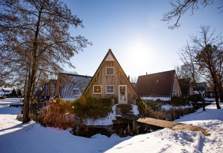 Casa pequeña Wellness Lodge cubierta de nieve en Hof van Salland, Países Bajos, con árboles al sol invernal.