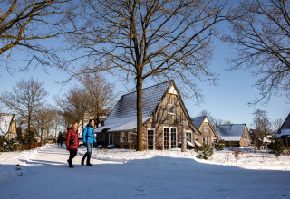 Dos personas caminan por la nieve frente a la tiny house Wellness Lodge en Hof van Salland, Países Bajos.