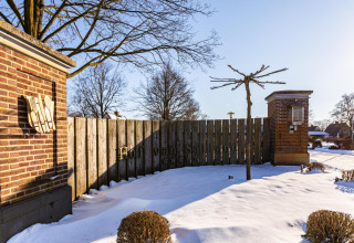 Entrée du Hof van Salland aux Pays-Bas, couverte de neige, avec des piliers en brique et des arbres derrière.