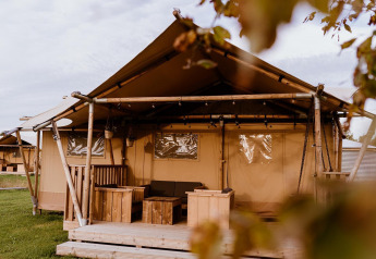 Tenda glamping accogliente con veranda in legno e area salotto, perfetta per una fuga nella natura.
