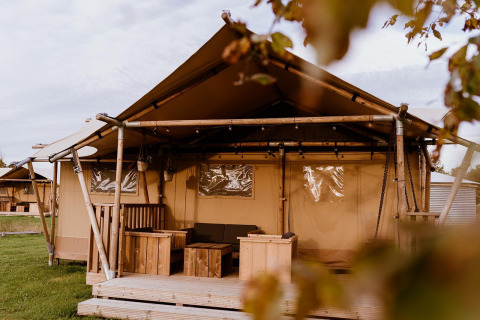 Gezellige glamping tent met houten terras en zitbanken, ideaal voor een luxueuze natuurvakantie.