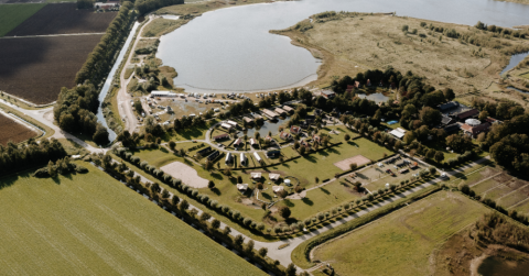 Vista aerea di un campeggio glamping con tende, lago, prati verdi e aree ricreative nella natura.