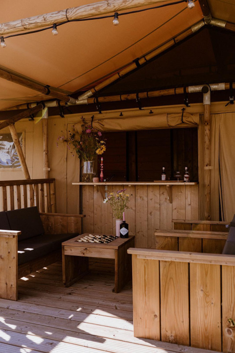 Interior de tienda de glamping tipo safari con muebles de madera y flores en Holiday park Eigen Wijze, Países Bajos.