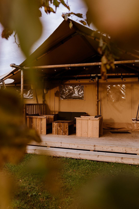 Vista de una tienda safari glamping con muebles de madera en Holiday park Eigen Wijze, Países Bajos, entre hojas.