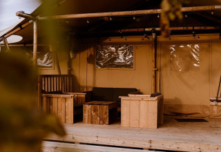 Vista de una tienda safari glamping con muebles de madera en Holiday park Eigen Wijze, Países Bajos, entre hojas.