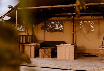 Vue d'une tente safari glamping avec meubles en bois à Holiday park Eigen Wijze, Pays-Bas, à travers des feuilles.