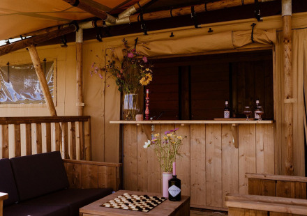 Buitengebied met bar in safaritent, houten meubels, bloemendecoratie en gezellige sfeer.
