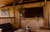 Outdoor bar area in a safari tent featuring wooden furniture, floral decor and a comfortable setting.