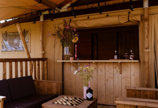 Outdoor bar area in a safari tent featuring wooden furniture, floral decor and a comfortable setting.