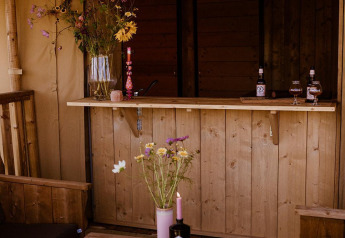 Tenda safari glamping al Holiday park Eigen Wijze nei Paesi Bassi, arredi rustici in legno e fiori selvatici.