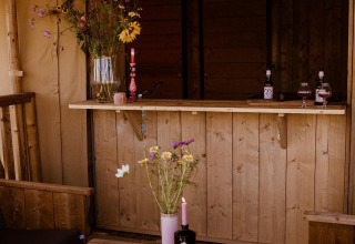 Glamping safaritent bij Holiday park Eigen Wijze in Nederland, met houten meubels en veldbloemen op tafel.