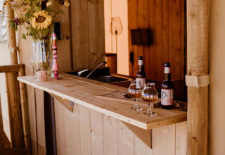 Bar exterior junto a una tienda safari con mostrador de madera, flores, botellas y copas sobre la barra.