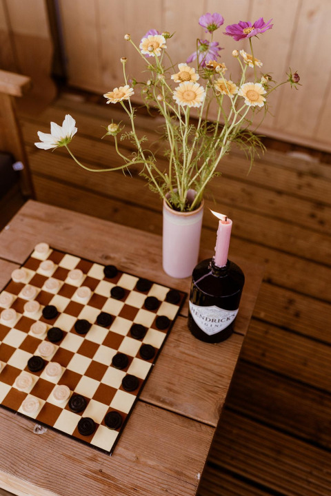 Foto di una scacchiera, fiori di campo in un vaso e una candela in una bottiglia in una tenda glamping nei Paesi Bassi.