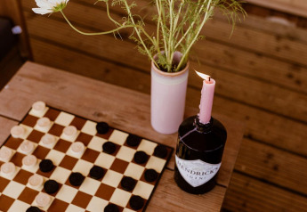 Foto de un tablero de damas, flores silvestres en un jarrón y una botella con vela en una tienda glamping en Países Bajos.