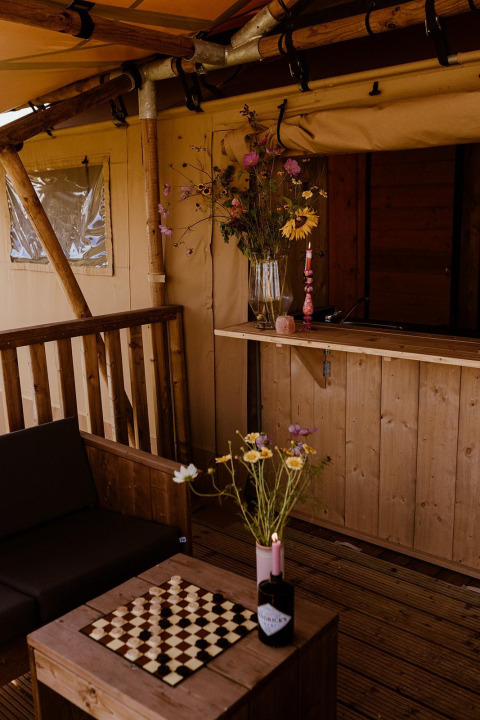 Acogedora tienda de glamping safari con muebles de madera, flores y ajedrez en Holiday Park Eigen Wijze.