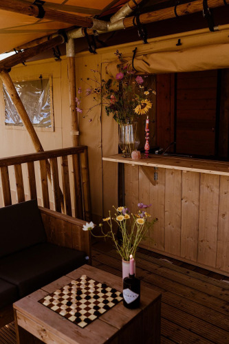 Knusse glamping-safaritent met houten meubels, bloemen en schaakbord bij Holiday park Eigen Wijze.