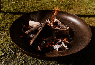 Hoguera ardiendo en un recipiente metálico junto a una tienda glamping en Holiday Park Eigen Wijze, Países Bajos.