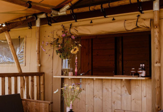 Udendørs siddeområde i en safaritelte med træmøbler, blomster og et skakbræt på bordet.